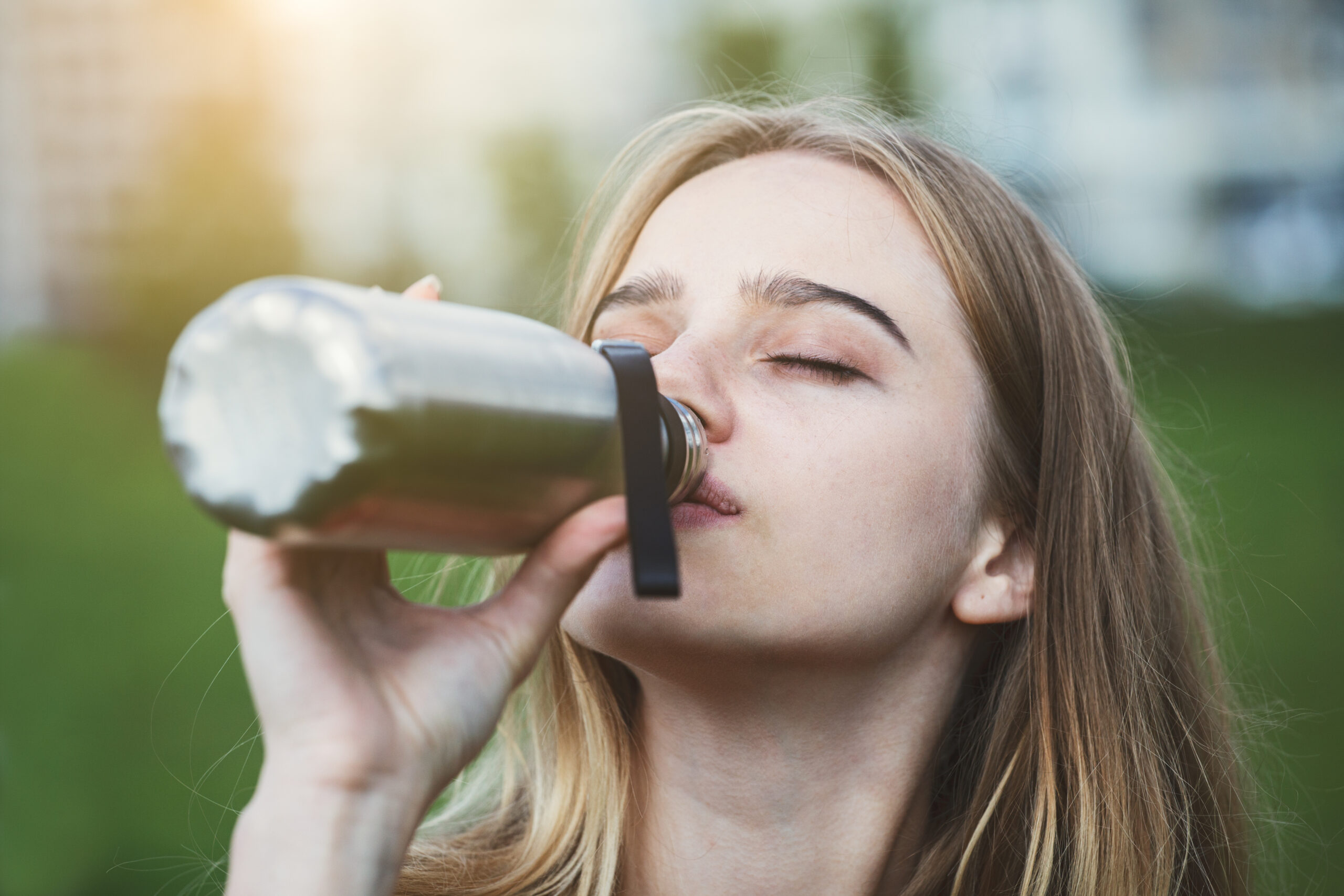 Photographie d'une jeune femme, les yeux fermés, en train de boire de l'eau dans une gourde.